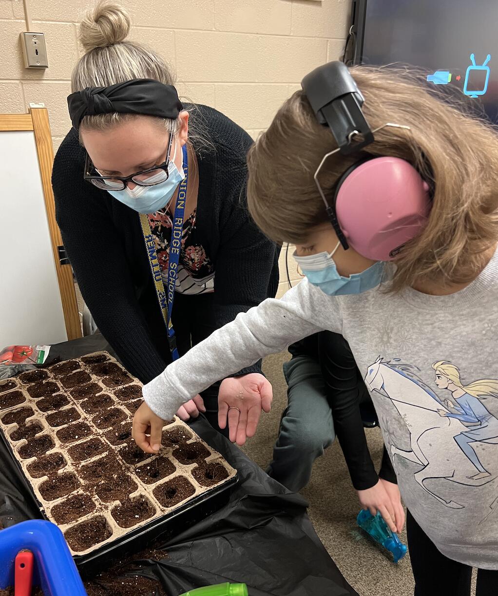Teacher, Ms. Ullmer, helping student, a girl, planting the seedlings