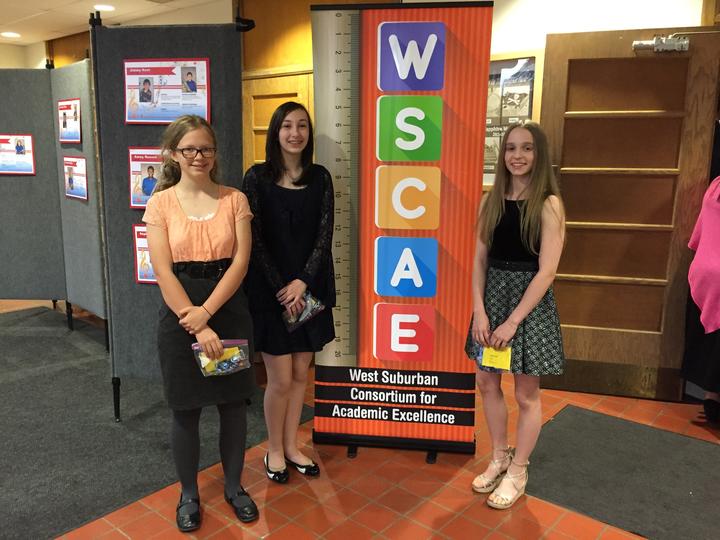 the winners, three girls, posing next to WSCAE banner