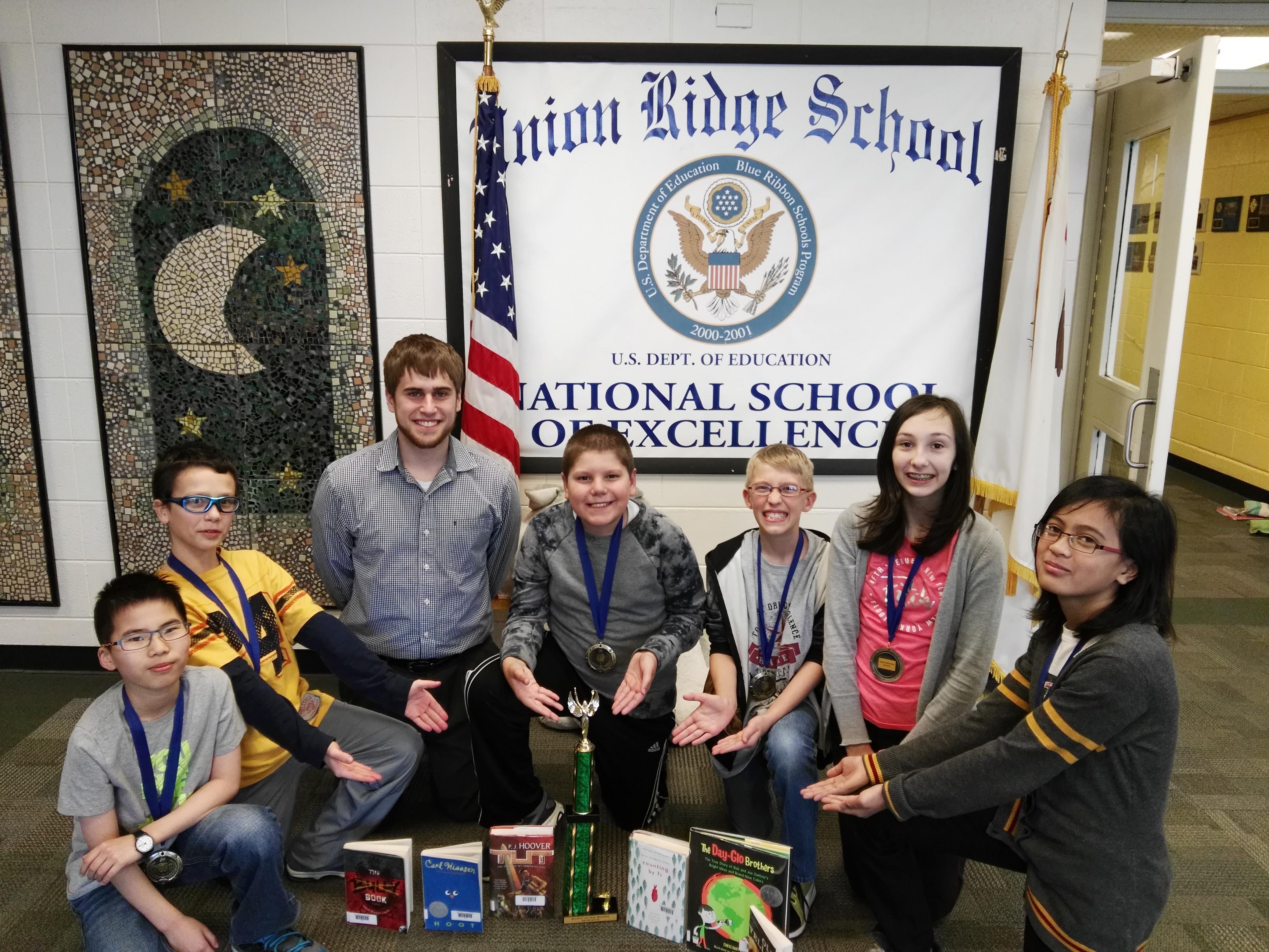 picture of students posing with a trophy and books